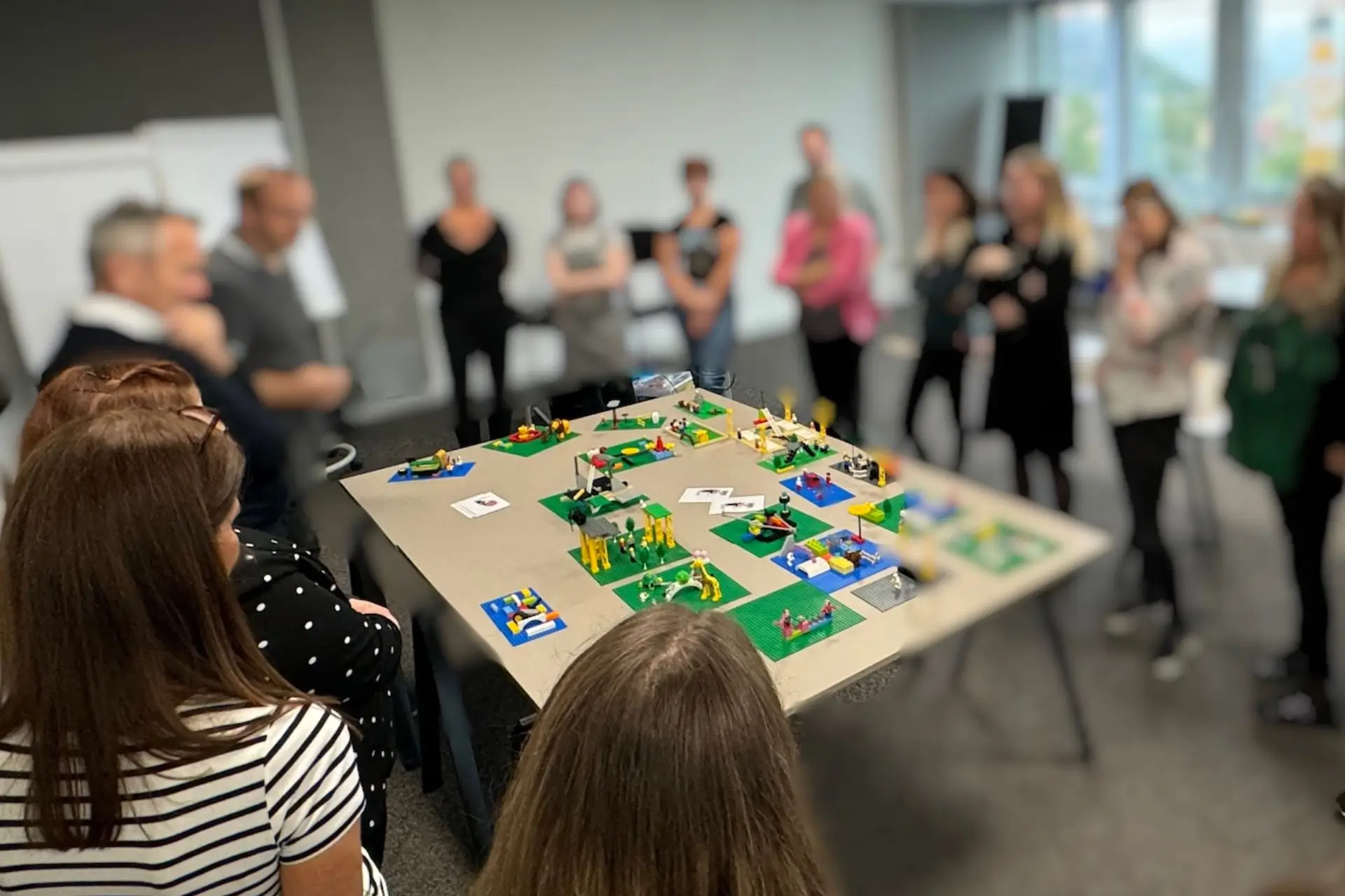 Workshop mit Lego Serious Play Trainer. Erwachsene Menschen stehen um Tisch auf dem Lego Modelle aufgebaut sind.