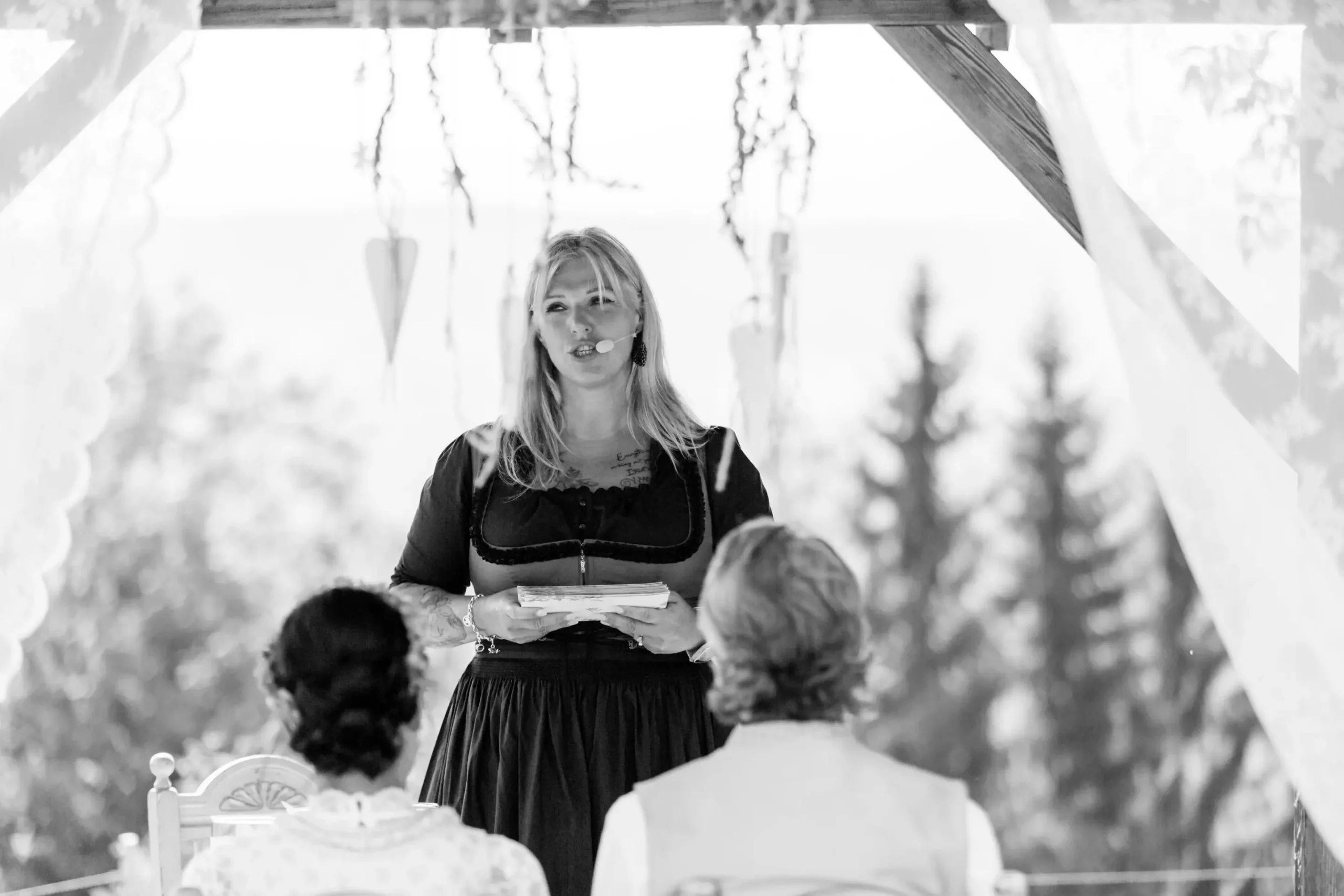 Heike Schönbacher spricht vor Brautpaar mit Mikrofon auf Terrasse schwarz-weiß