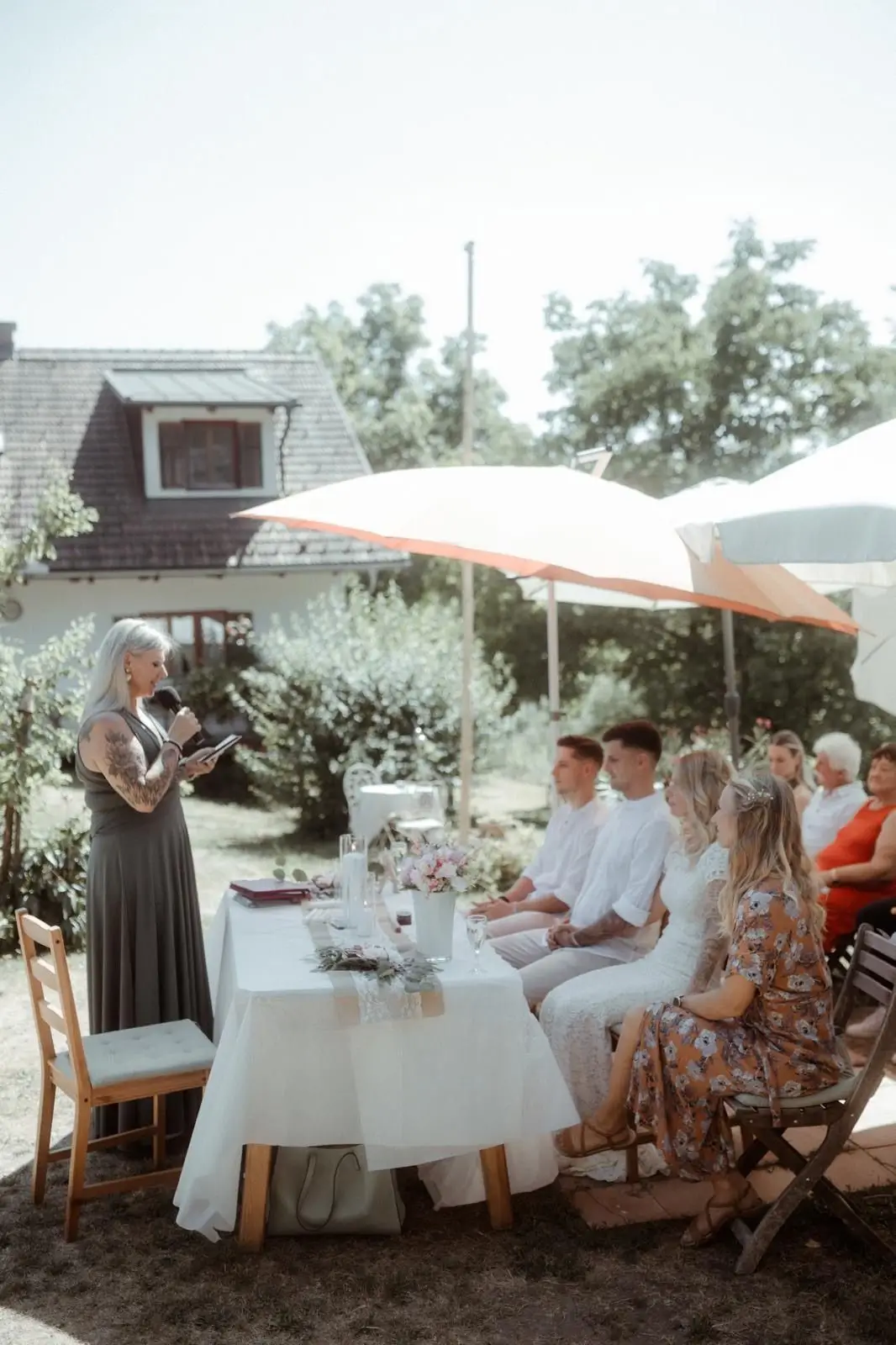 Gartenidylle mit Klappsesseln und Heike Schönbacher, die unter Sonnenschirm vor Hochzeitsgesellschaft spricht
