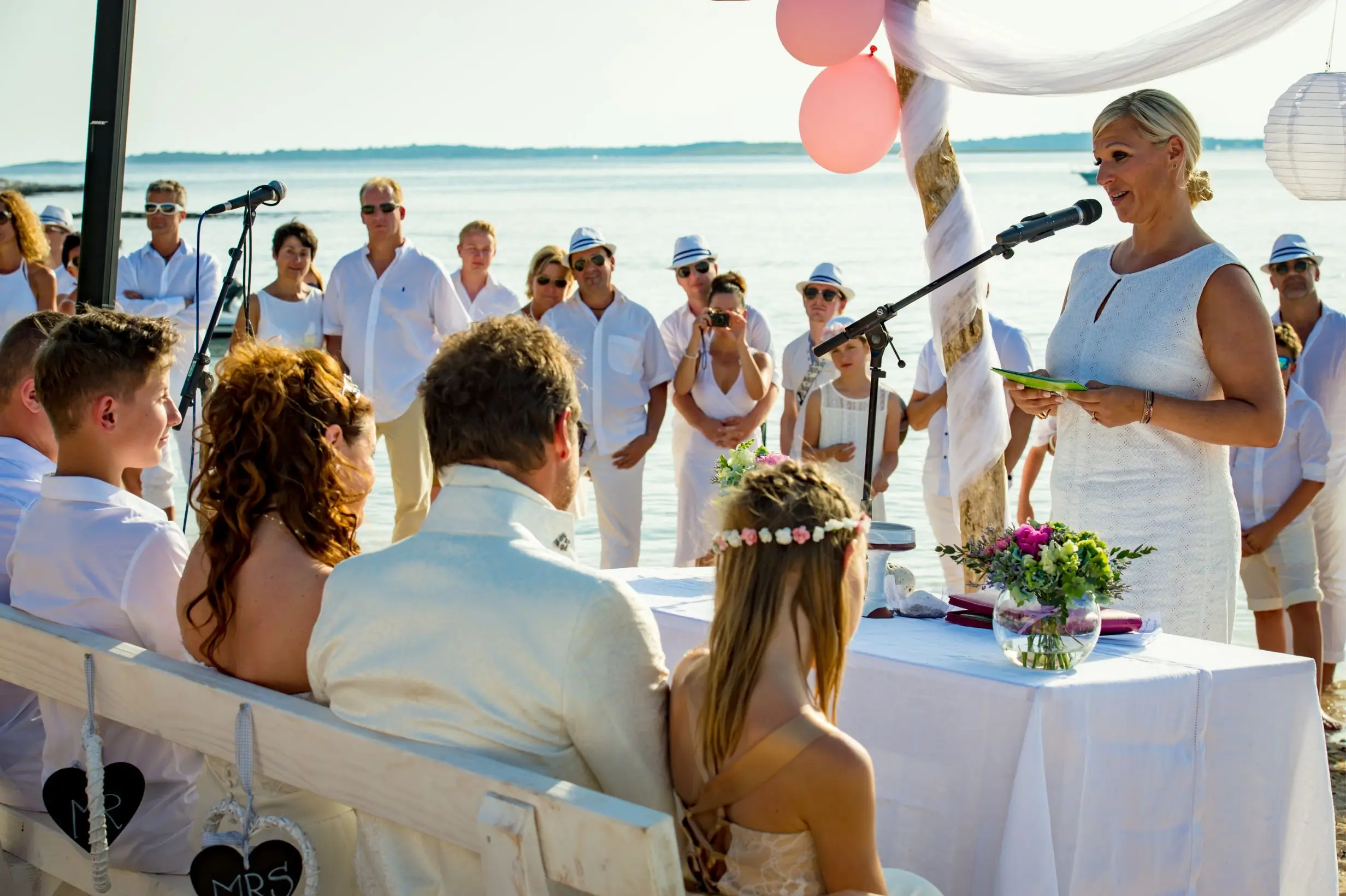 Hochzeitsgesellschaft in weißen Kleidern am Strand horcht der freien Rede von Heike Schönbacher