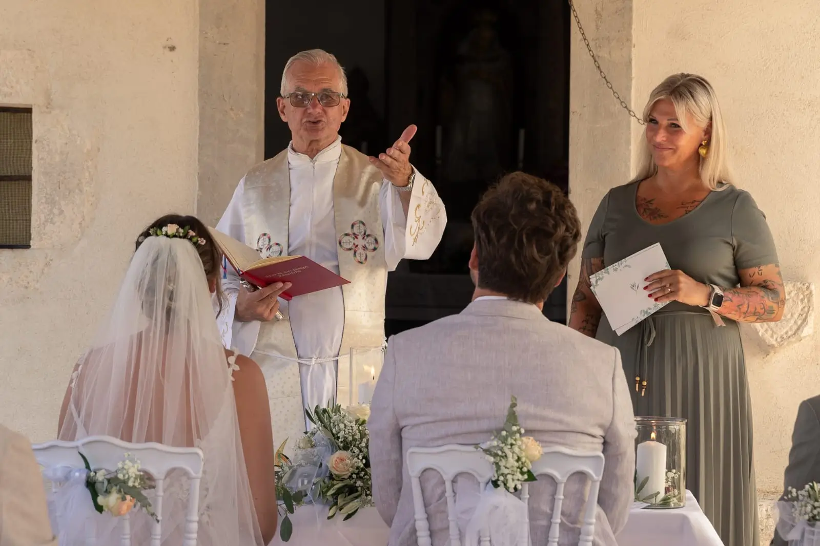 Freie Rednerin und kroatischer Pfarrer stehen gleichzeitig vor dem Hochzeitspaar während der Trauungs-Zeremonie